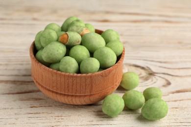 Tasty wasabi coated peanuts on white wooden table, closeup