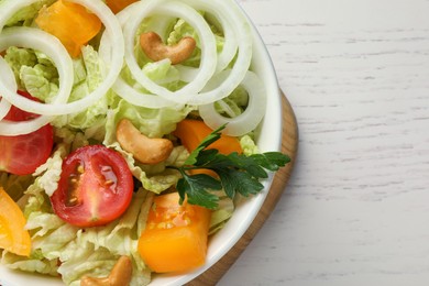 Bowl of delicious salad with Chinese cabbage, tomatoes, onion and parsley on white wooden table, top view. Space for text