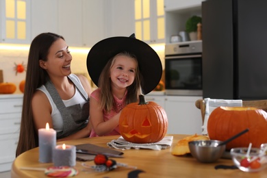 Photo of Mother and daughter with pumpkin jack o'lantern at table in kitchen. Halloween celebration