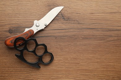 Black brass knuckles and knife on wooden background, flat lay. Space for text