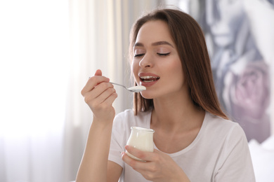 Young attractive woman eating tasty yogurt at home