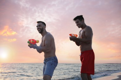 Friends with water guns having fun on beach at sunset