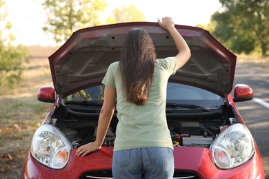 Young woman near broken car outdoors, back view