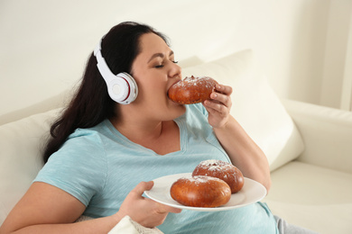 Lazy overweight woman with headphones eating bun at home