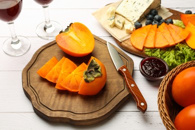 Photo of Delicious persimmon, blue cheese, blueberries and jam served on white wooden table, above view