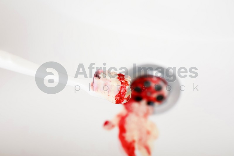 Photo of Toothbrush with paste and blood over sink, closeup. Gum inflammation