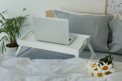 White tray table with laptop and bouquet of beautiful daisies on bed indoors