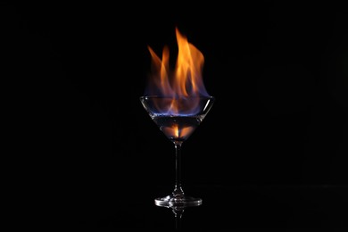 Cocktail glass with flaming vodka on black background