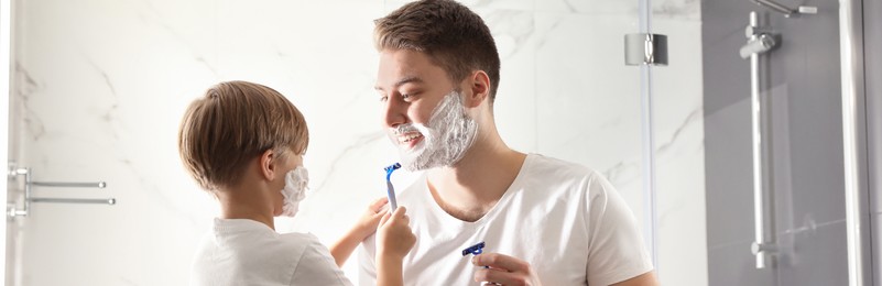 Dad and son with shaving foam on their faces having fun in bathroom. Banner design