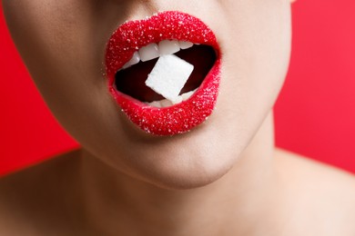 Woman with beautiful lips eating sugar cube on red background, closeup