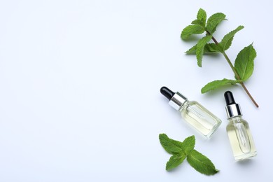Photo of Bottles of essential oil and mint on white background, flat lay. Space for text
