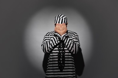 Prisoner in special uniform with chained hands on grey background