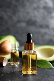 Bottle of essential oil and fresh avocado on black table