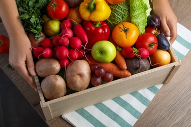 Farmer with crate full of different vegetables and fruits at wooden table, closeup. Harvesting time