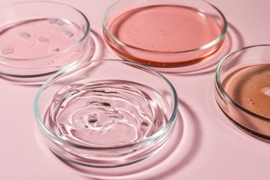 Photo of Petri dishes with liquids on pale pink background, closeup