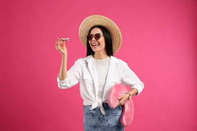 Photo of Happy female tourist with toy plane and travel pillow on pink background