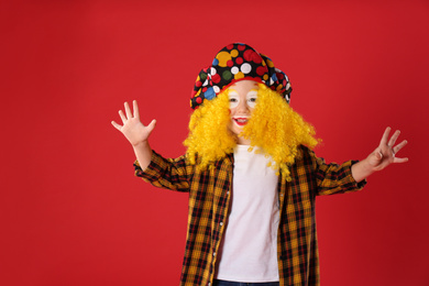 Photo of Funny little boy in clown costume on red background. April fool's day