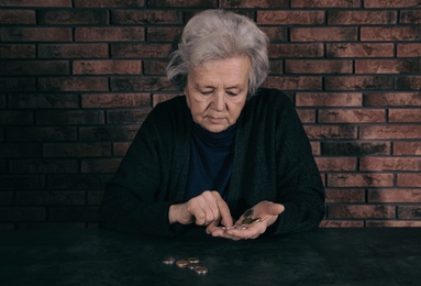 Poor mature woman counting coins at table