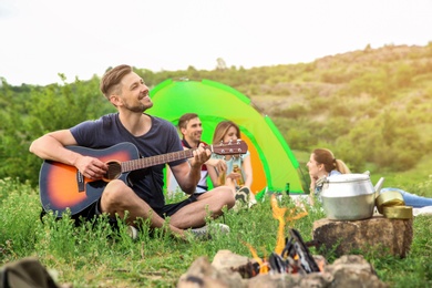 Man playing guitar near camping tent in wilderness