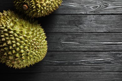 Ripe durians on black wooden table, flat lay. Space for text