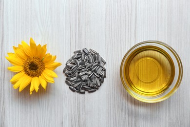 Cooking oil, sunflower seeds and flower on light wooden table, flat lay