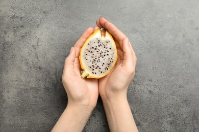 Photo of Woman holding fresh cut dragon fruit (pitahaya) on grey table, top view