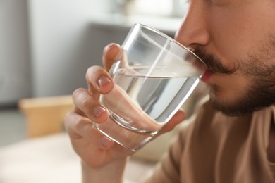 Man drinking water at home, closeup. Refreshing beverage
