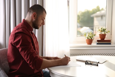 Man writing letter at white table in room