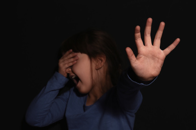 Crying little girl making stop gesture near black wall, focus on hand. Domestic violence concept