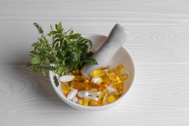 Photo of Mortar with fresh green herbs and pills on white wooden table, above view