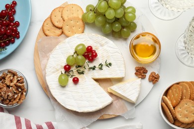 Brie cheese served with honey, berries and crackers on white table, flat lay