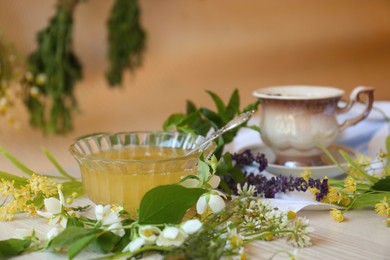 Cup of hot aromatic tea, honey and different fresh herbs on white wooden table