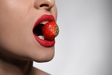Photo of Young woman with beautiful lips makeup eating strawberry on light background, closeup. Space for text