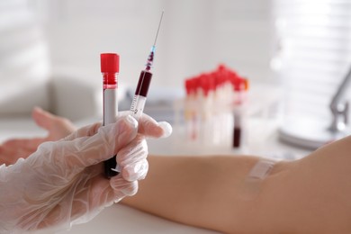 Nurse holding syringe and sample tube with blood in clinic, closeup. Space for text
