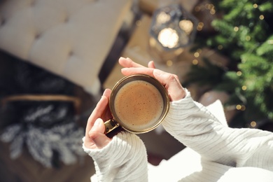 Woman with golden cup of hot drink in room decorated for Christmas, top view
