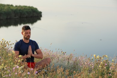 Man meditating in meadow near river. Space for text