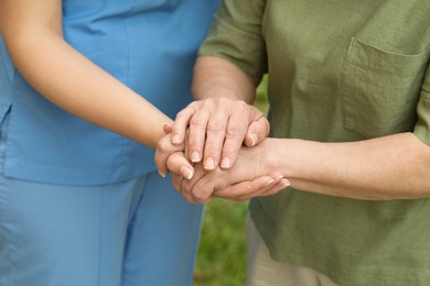 Elderly woman and female caregiver holding hands outdoors, closeup