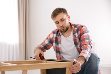 Young working man using measure tape at home, space for text