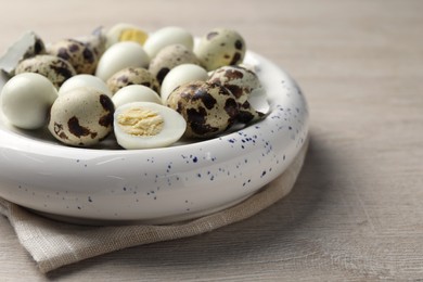 Photo of Unpeeled and peeled hard boiled quail eggs in bowl on white wooden table, closeup