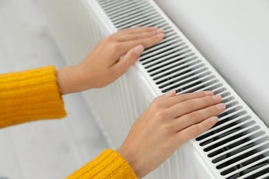 Woman warming hands on heating radiator indoors, closeup