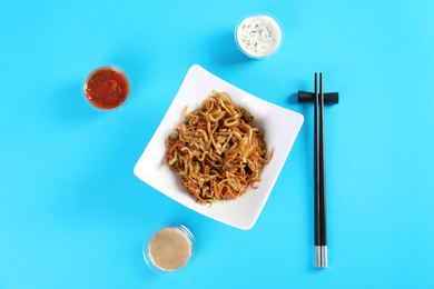 Photo of Chinese noodles served with chopsticks and different sauces on color background, top view. Food delivery