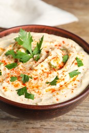 Tasty hummus with parsley and paprika in brown bowl on wooden table, closeup