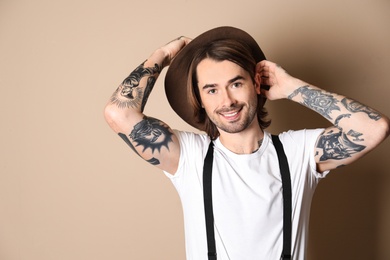 Young man with tattoos on arms against beige background