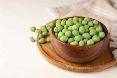 Tasty wasabi coated peanuts on white wooden table, space for text