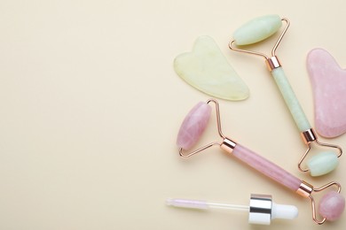 Gua sha tools, facial rollers and dropper on beige background, flat lay. Space for text