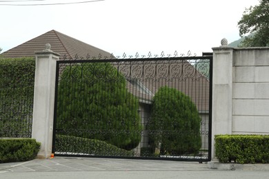 Photo of Beautiful stone fence with ornate black metal gates around house and garden