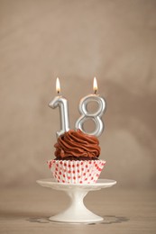 18th birthday. Delicious cupcake with number shaped candles for coming of age party on beige table