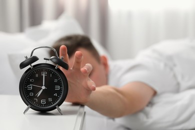 Photo of Man turning off alarm clock at home in morning, focus on hand. Space for text