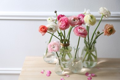 Beautiful ranunculus flowers on wooden table near wall. Space for text