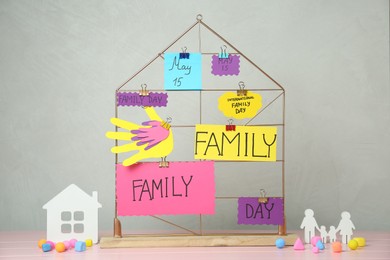 Photo of Paper cutouts and cards with text Family Day attached to decorative house on pink wooden table